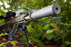 modern semi automatic rifle that has a silencer attached in the trees